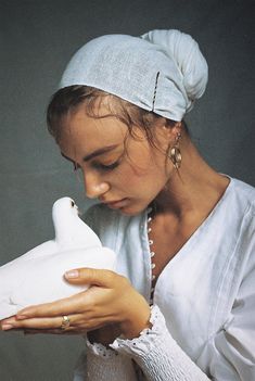 a woman holding a white bird in her right hand and looking down at it's beak