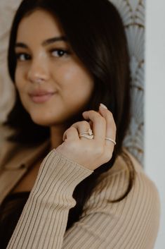 a woman wearing a tan sweater is smiling and holding her hand up to her ear