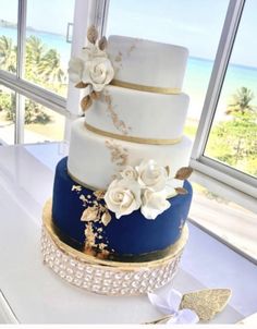 a three tiered wedding cake with white flowers on the top and gold trimmings