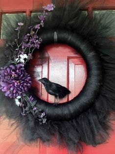 a black bird sitting on top of a wreath with purple flowers in front of it