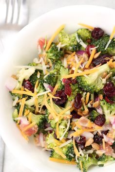 a white bowl filled with broccoli salad topped with cheese and cranberries