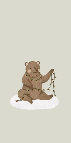 a brown teddy bear sitting on top of a snow covered ground holding a string of lights