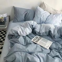 an unmade bed with blue sheets and pillows on top of it next to a checkered nightstand