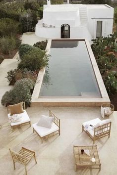 an outdoor swimming pool surrounded by lounge chairs and tables with pillows on the floor next to it