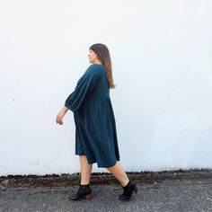 a woman is walking down the street wearing black shoes and a green shirtdress