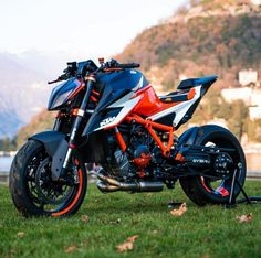 an orange and black motorcycle parked on top of a lush green field next to a body of water