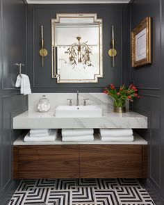 a bathroom with gray walls and white counter tops, gold framed mirror above the sink