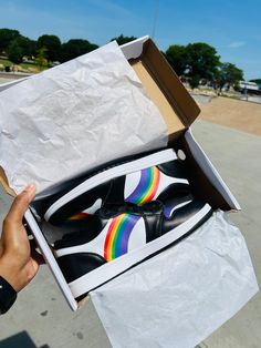 someone is holding up a pair of sneakers in a box on the street with a rainbow painted shoe inside