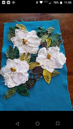 an appliqued piece of cloth with white flowers on blue fabric and green leaves