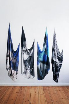 four scarves hanging on the wall in front of a wooden floor and white wall