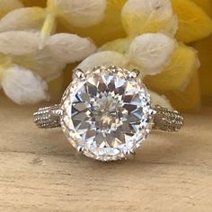 a diamond ring sitting on top of a wooden table next to yellow and white flowers