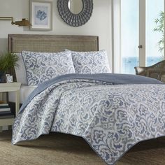 a blue and white comforter set on a bed in a room with an ocean view