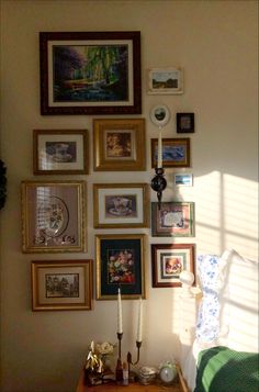 a wall filled with lots of framed pictures next to a lamp on a wooden table