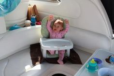 a baby sitting in a highchair on the back of a boat with its arms up