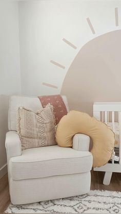 a baby's room with a white crib, chair and sun wall decal