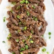 a white plate topped with sliced beef and green onions on top of mashed potatoes