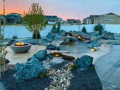 an outdoor fire pit surrounded by rocks and gravel at dusk with the sun setting in the background