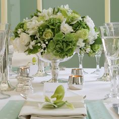 the table is set with white and green flowers in vases, napkins, silverware, and candles