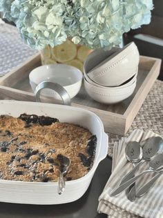 a blueberry cobbler in a white dish on a tray next to silverware