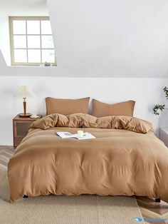 a bed with brown sheets and pillows in a room next to a lamp on a table