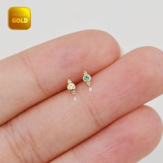 a person's hand holding two tiny earrings in their left hand, with the word gold on it