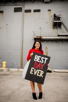 a woman holding a sign that says best day ever in front of a large ship