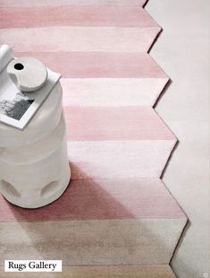 a white vase sitting on top of a pink and white striped rug next to a toilet paper dispenser