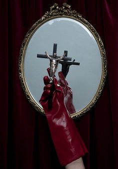 a person wearing red gloves holding up a cross in front of a mirror