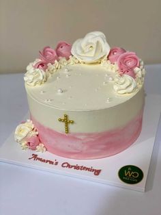 a cake with white and pink frosting on top is decorated with flowers and a cross