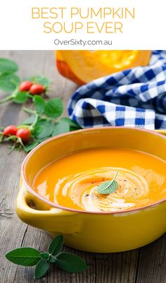 a yellow bowl filled with carrot soup on top of a wooden table next to vegetables