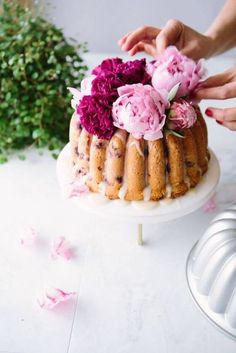 someone is decorating a cake with flowers on the top and frosting around it