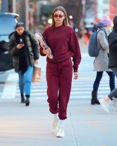 a woman walking down the street in a maroon outfit with white sneakers and holding a cell phone