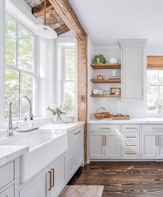 a kitchen with white cabinets and wooden shelves on the wall, along with open windows