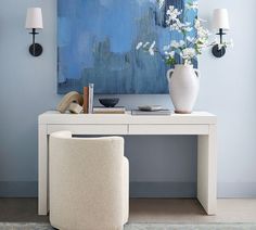 a white desk and chair in front of a blue painting