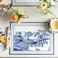 the table is set with blue and white plates, silverware, tea cups, and flowers