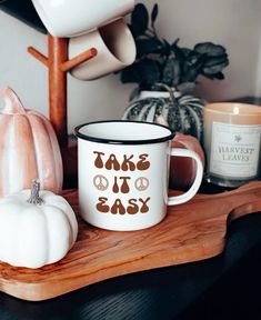 there is a coffee cup that says take it easy on the table next to some pumpkins