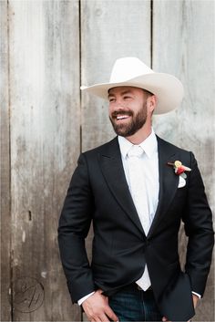 a man in a black suit and white cowboy hat standing next to a wooden fence