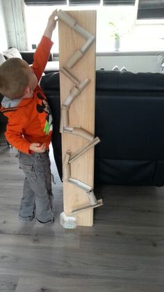 a young boy standing next to a tall wooden board on top of a hard wood floor