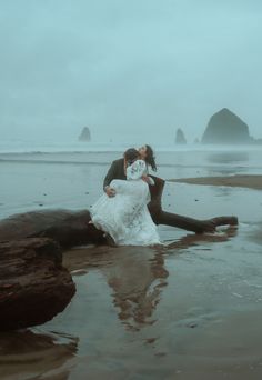 a bride and groom kissing on the beach in front of hays rock formations at low tide