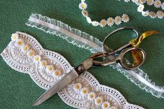 pair of scissors and lace on green surface with daisies in the background, closeup