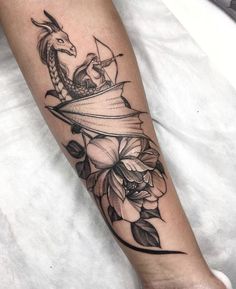 a woman's arm with a dragon on top of it and flowers around it