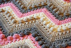 a crocheted blanket is shown in pink, brown and white colors with an interesting chevron design