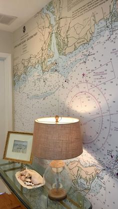 a glass table topped with a lamp next to a wall covered in nautical map paper