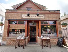 the outside of a book store with two chairs in front of it and a sign on the door that says visible voice books