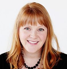 a woman with long red hair wearing a black shirt and necklace smiling at the camera