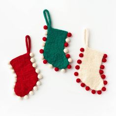 three felt christmas stockings with pom - poms hanging from the sides on a white background