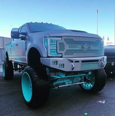 a large truck with big tires parked in a parking lot next to other cars and trucks