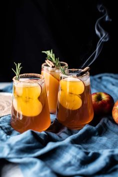 two glasses filled with apple cider on top of a blue blanket next to apples