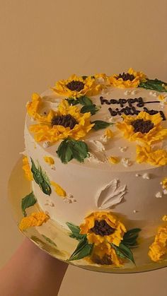 a cake with sunflowers on it being held up by someone's hand