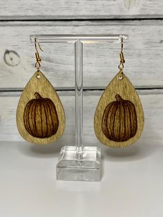 a pair of wooden earrings with an orange design on them, sitting on a stand